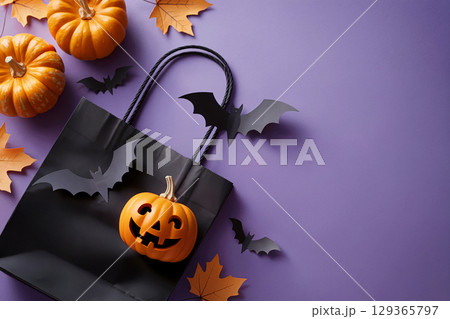 Halloween black gift bag with pumpkin and flying bats surrounded by fall leaves on purple background 129365797