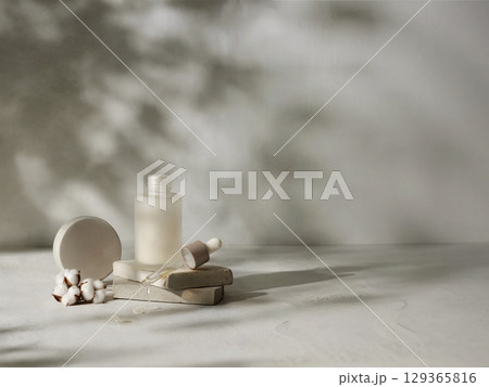 Open cosmetic serum bottle with dropper on stone slab with cotton flower in soft light and natural shadows 129365816