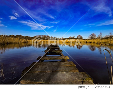 Old Wooden Pier on Calm Lake Under Vibrant Blue Sky Old Wooden Pier on Calm Lake Under Vibrant Blue Sky 129366503