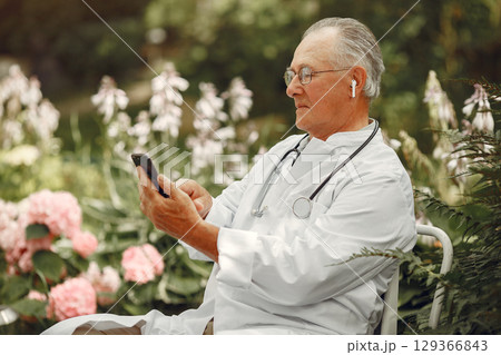 Technology, people and communication concept. Senior man at summer park. Doctor using a phone. 129366843