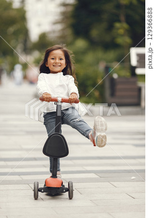 Child on kick scooter in park. Kids learn to skate roller board. Little girl skating on sunny summer day. 129366888