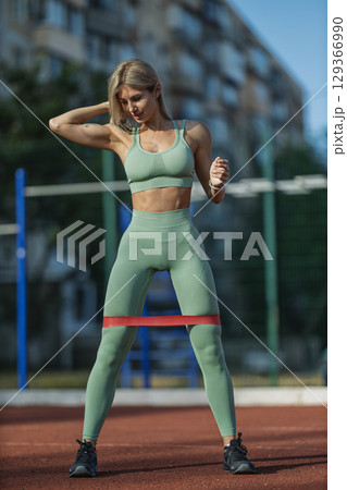 sporty girl wearing a green athletic outfit performs resistance band exercises at an outdoor gym 129366990