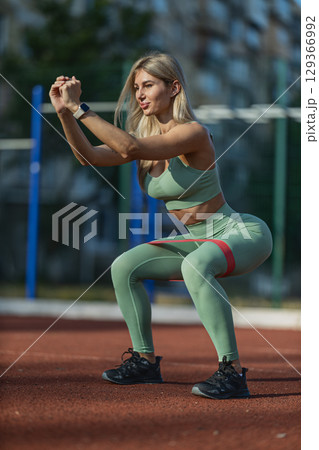 girl in athletic attire is engaged in squat exercises on a red track in an outdoor fitness area She is focused and determined, showcasing her sporty energy and workout routine 129366992