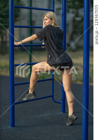 woman is actively using outdoor fitness equipment in a park, demonstrating her strength and agility while wearing comfortable athletic clothing in the bright daylight woman is actively using outdoor fitness equipment in a park, demonstrating her strength and agility while wearing comfortable athletic clothing in the bright daylight 129367035