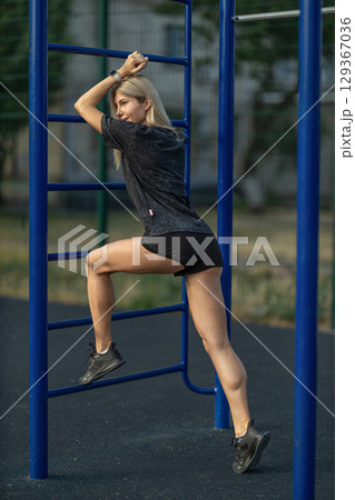 woman engages in a strength training workout on outdoor equipment at a park She demonstrates agility and determination while climbing the bars, showcasing her fitness routine woman engages in a strength training workout on outdoor equipment at a park She demonstrates agility and determination while climbing the bars, showcasing her fitness routine 129367036
