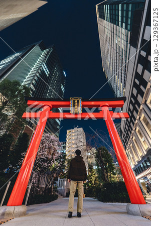 高層ビルに囲まれた福徳神社の赤い鳥居（夜景）と人の後ろ姿 129367125