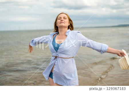 Happy woman at the seaside, enjoying her vacation. Cloudy day. 129367183