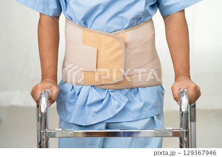 Asian senior pain back wearing elastic support belt with walker. 129367946