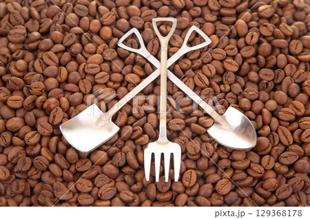 Elegant still life featuring two crossed metal shovels surrounded by roasted coffee beans 129368178