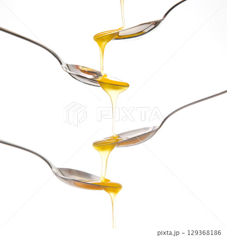 A striking image of golden honey cascading from one metal spoon  129368186