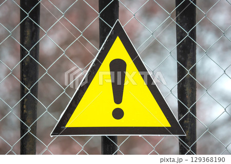 warning sign in the form of a triangle on a metal mesh fence warning sign in the form of a triangle on a metal mesh fence 129368190
