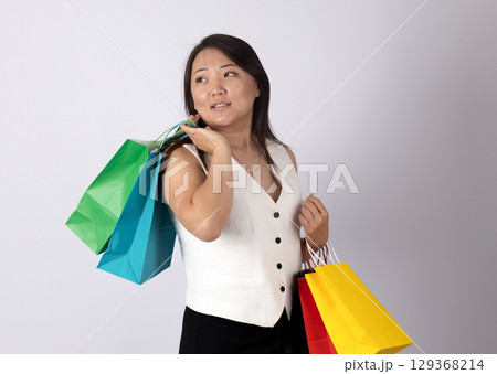 An asian woman standing against a plain, light background, holding several shopping bags 129368214
