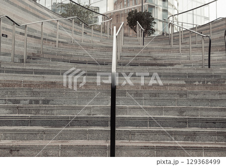 Perspective view of outdoor steps that become walls with stainless steel sleek railings handle grip of leading to entrance into modern building. Perspective view of outdoor steps that become walls with stainless steel sleek railings handle grip of leading to entrance into modern building. 129368499