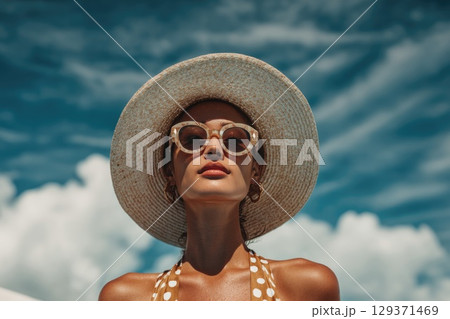 beautiful woman wearing sunglasses and a hat is standing by the pool, with a blue sky and white clouds in the background 129371469