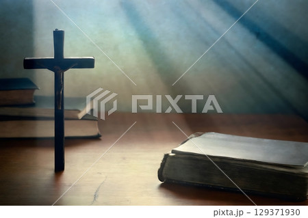 Cross on Table with Holy Bible and Books Surrounded by Rays of Light in Spiritual Setting 129371930