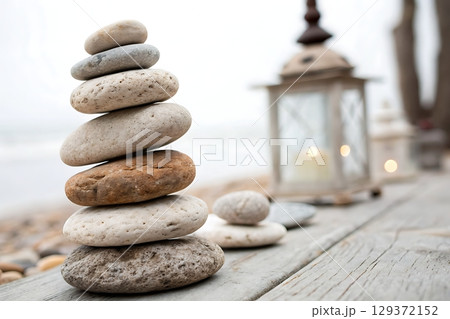 Tranquil Arrangement of Smooth Stones Near a Lantern on a Beachside Wooden Surface 129372152