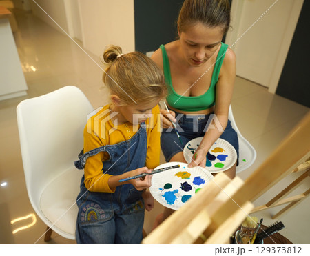 A mother and her daughter are engaged in a painting session  129373812