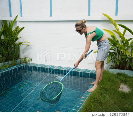 A young woman clean leaves out of a pool  129373844