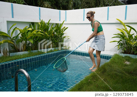 A young woman clean leaves out of a pool A young woman clean leaves out of a pool 129373845