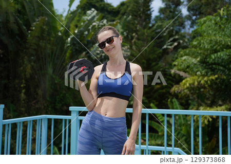 A young woman is training outdoors with dumbbells  129373868