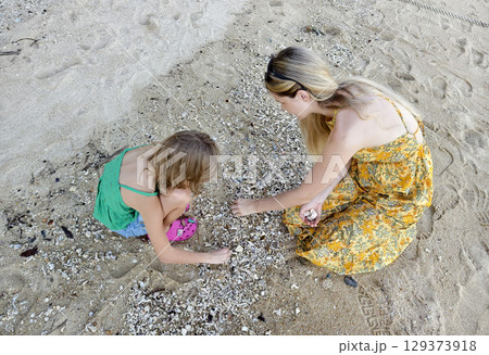 A mother and her daughter as they collect shells together  129373918
