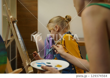 A mother and her daughter are engaged in a painting session A mother and her daughter are engaged in a painting session 129374564