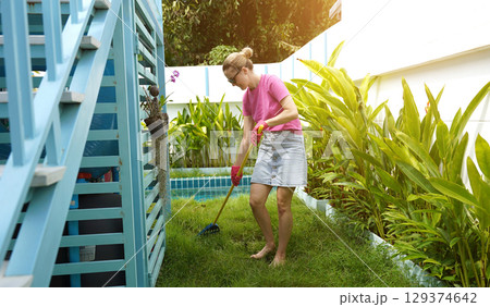A woman raking the lawn at the backyard of her house A woman raking the lawn at the backyard of her house 129374642