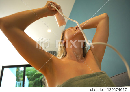A woman is expertly styling her hair using a blow dryer and brush while in the bathroom A woman is expertly styling her hair using a blow dryer and brush while in the bathroom 129374657