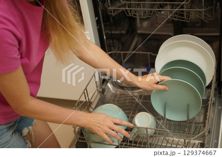 Young woman takes dishes out of the dishwasher machine Young woman takes dishes out of the dishwasher machine 129374667