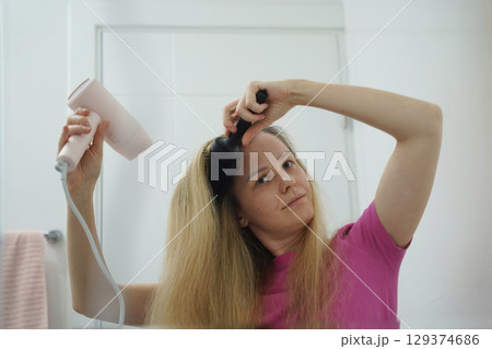 A woman is expertly styling her hair using a blow dryer and brush while in the bathroom 129374686