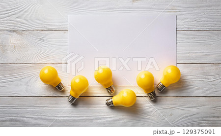Bright Yellow Light Bulbs and Blank White Paper on Rustic Wooden Background for Creative Ideas 129375091