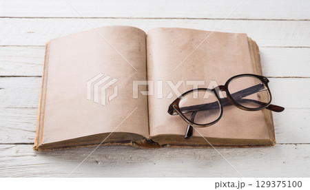 Old Open Vintage Book with Classic Reading Glasses on White Wooden Background Nostalgic Literature Concept Old Open Vintage Book with Classic Reading Glasses on White Wooden Background Nostalgic Literature Concept 129375100