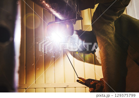 Worker in safety mask welds metal at industrial enterprises. Worker in safety mask welds metal at industrial enterprises. 129375799