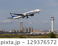 管制塔をバックに離陸する飛行機 129376572