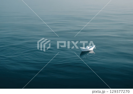 Small Paper Boat Floating on Vast Reflective Water Surface in Tranquil Environment 129377270