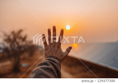 Hand Reaching Out to Touch Glowing Solar Panel Under Beautiful Sunset Sky 129377380
