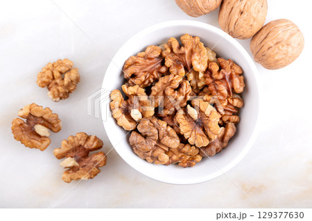 Walnut kernel halves, in a white bowl, on a marble surface. Shelled and dried halves of walnut kernels, seeds of common walnut tree, Juglans regia, used as snack or for baking. Close-up, from above. Walnut kernel halves, in a white bowl, on a marble surface. Shelled and dried halves of walnut kernels, seeds of common walnut tree, Juglans regia, used as snack or for baking. Close-up, from above. 129377630