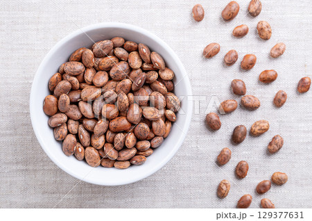 Pinto beans, in a white bowl, on linen fabric. Dried variety of common beans, Phaseolus vulgaris. Type of bean that are tan with reddish-brown specks. Most popular bean in Mexico and Southwestern USA. 129377631