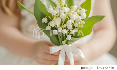 Chrismation symbol as young girls hands gently hold lilies of the valley flowers bouquet with white ribbon 129378716