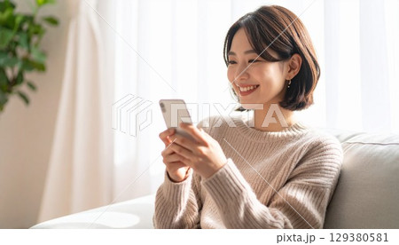 柔らかな日が差すリビングルームでスマートフォンを操作する若くて美しい日本人女性 129380581