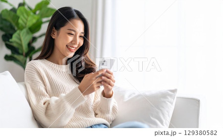 柔らかな日が差すリビングルームでスマートフォンを操作する若くて美しい日本人女性 129380582