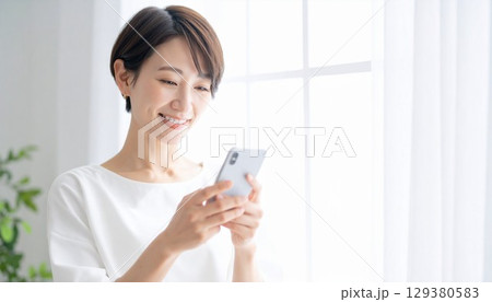 柔らかな日が差すリビングルームでスマートフォンを操作する若くて美しい日本人女性 129380583