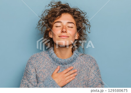 Young woman with closed eyes and hand on chest 129380675