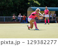Field hockey player hitting the ball under the bright sun during a game 129382277