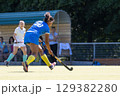 Competitive field hockey match featuring players in action at a sunny outdoor venue 129382280