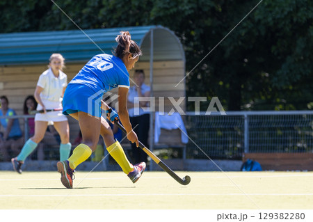 Competitive field hockey match featuring players in action at a sunny outdoor venue Competitive field hockey match featuring players in action at a sunny outdoor venue 129382280