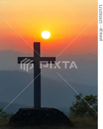 A crucifix stands majestically against a vibrant mountain sunset in the evening sky 129382571