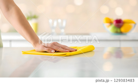 Cleaning a kitchen countertop with a yellow cloth during a bright, sunny day 129383483
