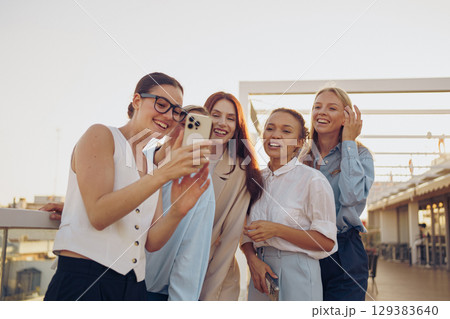 A joyful group of friends happily taking a cheerful selfie outdoors, smiling and laughing 129383640