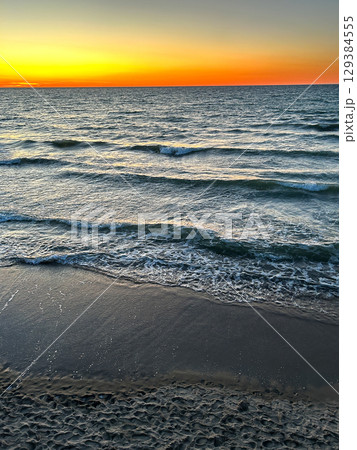Sunset gradient from blue to orange above blue ocean water with small waves. 129384555